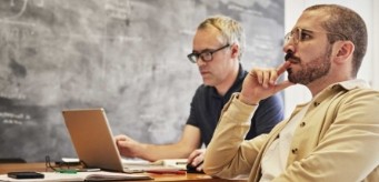 Two individuals sitting next to a chalkboard.