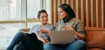 Two individuals having a conversation while sitting next to each other with their laptops.