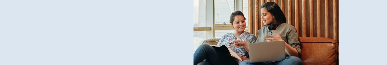 Two women discuss something over a laptop in an informal office setting.